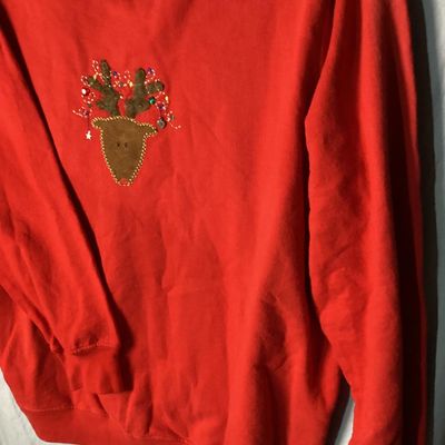 Sale Photo Thumbnail #11: Red long-sleeve crewneck sweatshirt featuring a center front embroidered and embellished reindeer applique with holiday light details. Measures approximately 28 to 29 inches in length as shown against the tape measure. Pre-owned condition with light signs