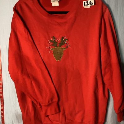 Sale Photo Thumbnail #10: Red long-sleeve crewneck sweatshirt featuring a center front embroidered and embellished reindeer applique with holiday light details. Measures approximately 28 to 29 inches in length as shown against the tape measure. Pre-owned condition with light signs