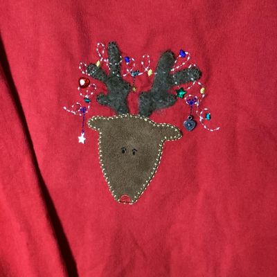 Sale Photo Thumbnail #12: Red long-sleeve crewneck sweatshirt featuring a center front embroidered and embellished reindeer applique with holiday light details. Measures approximately 28 to 29 inches in length as shown against the tape measure. Pre-owned condition with light signs