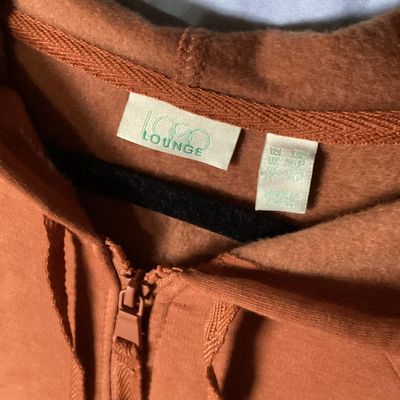 Sale Photo Thumbnail #68: LOGO Lounge by Lori Goldstein longline zip-up hoodie in a rust/terracotta shade. Features a hooded neckline with drawstring, front zip closure, front patch pockets, long sleeves, and a high-low hem. Lightly used condition with no visible damage or severe 