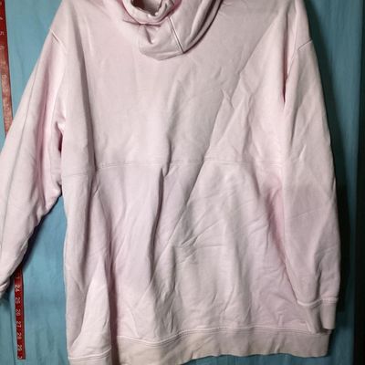 Sale Photo Thumbnail #90: Light pink long-sleeve hoodie by Nike featuring a prominent black graphic Swoosh logo on the front chest, drawstring hood, and ribbed cuffs and hem. Pre-owned condition with light fabric creasing and faint surface marks visible upon close inspection. Leng
