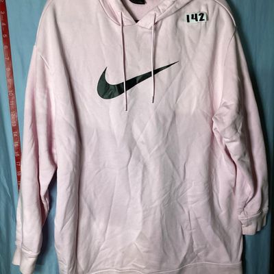 Sale Photo Thumbnail #88: Light pink long-sleeve hoodie by Nike featuring a prominent black graphic Swoosh logo on the front chest, drawstring hood, and ribbed cuffs and hem. Pre-owned condition with light fabric creasing and faint surface marks visible upon close inspection. Leng