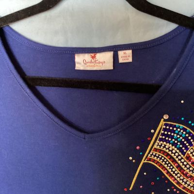 Sale Photo Thumbnail #137: Quacker Factory short sleeve V-neck top in blue, featuring a embellished American flag design on the chest with colorful rhinestones and studs. Tagged size XL. Made in China. Measures approximately 28 inches in length from shoulder to hem. Good pre-owned 