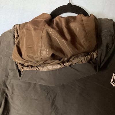 Sale Photo Thumbnail #176: Volcom hooded jacket in dark brown with bright orange and yellow patterned interior lining. Features zip-up and hook-and-loop closures, multiple cargo and zipper pockets, powder skirt, and underarm zip vents. Marked size Youth Large (L). Overall good pre-