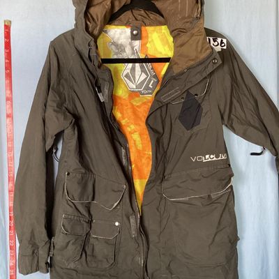 Sale Photo Thumbnail #168: Volcom hooded jacket in dark brown with bright orange and yellow patterned interior lining. Features zip-up and hook-and-loop closures, multiple cargo and zipper pockets, powder skirt, and underarm zip vents. Marked size Youth Large (L). Overall good pre-