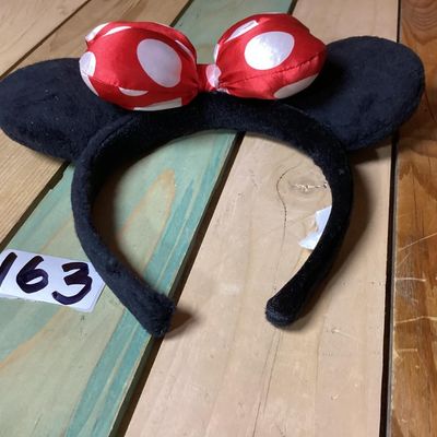 Sale Photo Thumbnail #218: Minnie Mouse themed headband featuring black plush mouse ears and a red bow with white polka dots. Fabric-wrapped headband. Measures approximately 10 inches wide by 8 inches tall. In good pre-owned condition with intact tag.