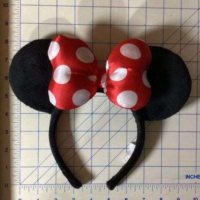 Sale Photo Thumbnail #216: Minnie Mouse themed headband featuring black plush mouse ears and a red bow with white polka dots. Fabric-wrapped headband. Measures approximately 10 inches wide by 8 inches tall. In good pre-owned condition with intact tag.