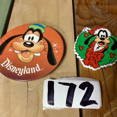 Sale Photo Thumbnail #268: Pair of vintage Goofy collectible pins/brooches featuring:
- A large circular Disneyland button pin featuring Goofy's face, measuring approximately 3 inches in diameter. Has light adhesive residue on the back.
- A plastic/molded Christmas wreath brooch fe