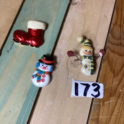 Sale Photo Thumbnail #271: A festive collection of three Christmas-themed brooches and pins. Includes a red enameled Santa boot/stocking brooch, a painted plastic snowman wearing a black top hat, and a textured resin/painted snowman pin with wire-articulated mitten arms. Each pin m