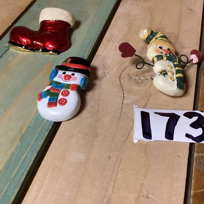 Sale Photo Thumbnail #272: A festive collection of three Christmas-themed brooches and pins. Includes a red enameled Santa boot/stocking brooch, a painted plastic snowman wearing a black top hat, and a textured resin/painted snowman pin with wire-articulated mitten arms. Each pin m