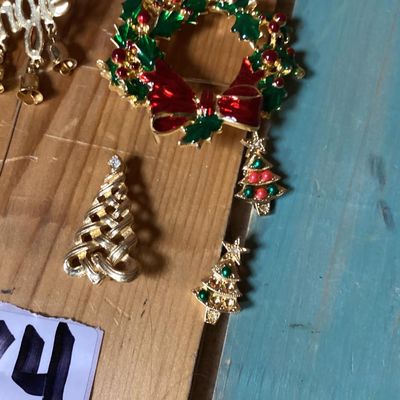 Sale Photo Thumbnail #277: Collection of festive Christmas-themed fashion jewelry, including:
- Enamel wreath brooch with red bow accent and dangling Christmas tree
- Gold-tone 'Jingle' pin with dangling bell charms
- Gold-tone woven Christmas tree brooch with rhinestone top
- Two 