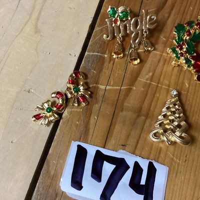 Sale Photo Thumbnail #279: Collection of festive Christmas-themed fashion jewelry, including:
- Enamel wreath brooch with red bow accent and dangling Christmas tree
- Gold-tone 'Jingle' pin with dangling bell charms
- Gold-tone woven Christmas tree brooch with rhinestone top
- Two 