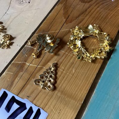 Sale Photo Thumbnail #283: Collection of festive Christmas-themed fashion jewelry, including:
- Enamel wreath brooch with red bow accent and dangling Christmas tree
- Gold-tone 'Jingle' pin with dangling bell charms
- Gold-tone woven Christmas tree brooch with rhinestone top
- Two 