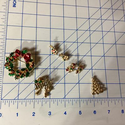 Sale Photo Thumbnail #284: Collection of festive Christmas-themed fashion jewelry, including:
- Enamel wreath brooch with red bow accent and dangling Christmas tree
- Gold-tone 'Jingle' pin with dangling bell charms
- Gold-tone woven Christmas tree brooch with rhinestone top
- Two 