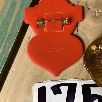 Sale Photo Thumbnail #288: Pair of vintage brooches including:
- 1983 Hallmark Cards, Inc. plastic/enamel heart pin that reads "Most Marvelous Mom". Measures approximately 2.25 inches tall.
- Red glitter enamel and rhinestone gold-tone apple brooch. Measures approximately 1.25 inch