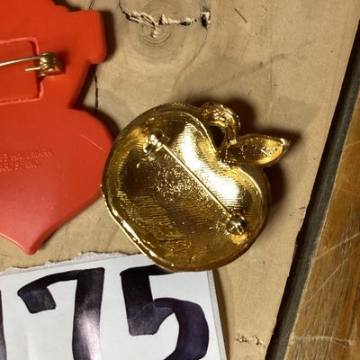 Sale Photo Thumbnail #289: Pair of vintage brooches including:
- 1983 Hallmark Cards, Inc. plastic/enamel heart pin that reads "Most Marvelous Mom". Measures approximately 2.25 inches tall.
- Red glitter enamel and rhinestone gold-tone apple brooch. Measures approximately 1.25 inch
