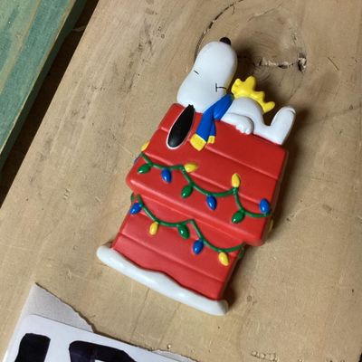 Sale Photo Thumbnail #292: Vintage Hallmark Cards Peanuts collectible lapel pin featuring Snoopy and Woodstock sleeping atop a red doghouse decorated with Christmas lights. Marked on back '© UFS HMK. CDS.' Pin clasp on back intact. Measures approximately 2 inches tall. In good pre