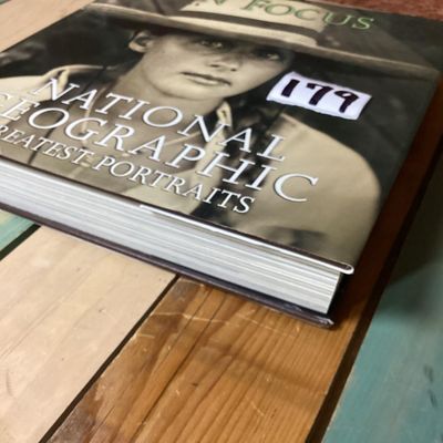 Sale Photo Thumbnail #303: Hardcover photography book titled 'In Focus: National Geographic Greatest Portraits'. Features 280 portrait photographs spanning over a century. Includes original dust jacket. Dust jacket shows some wear and a tear on the back corner, but internal pages r