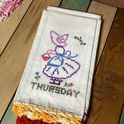 Sale Photo Thumbnail #321: Set of vintage white cotton kitchen/tea towels featuring cross-stitched embroidered designs for days of the week (Sunday through Saturday). Each towel depicts a Sunbonnet Sue/chores motif with colorful crocheted lace trim at the bottom hem. Appears to be 
