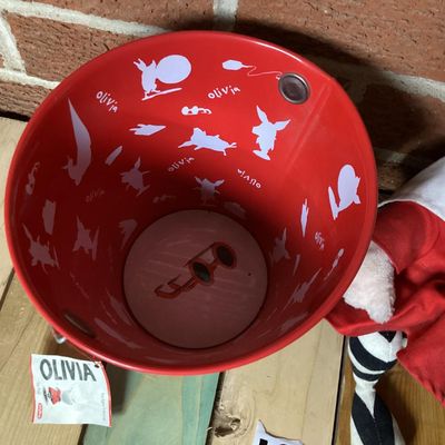 Sale Photo Thumbnail #325: Collection of vintage Olivia the Pig items featuring a GUND plush doll wearing a red dress with original tags attached and a matching Schylling red tin pail with handle and original tag attached (dated 2003). Both items are in good overall condition with 