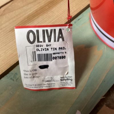 Sale Photo Thumbnail #330: Collection of vintage Olivia the Pig items featuring a GUND plush doll wearing a red dress with original tags attached and a matching Schylling red tin pail with handle and original tag attached (dated 2003). Both items are in good overall condition with 