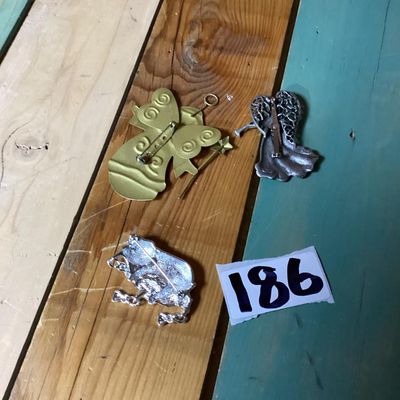 Sale Photo Thumbnail #355: Lot of 3 decorative brooches featuring an angel with a trumpet, a painted angel holding a wand/star, and a silver-tone pig figure. Each piece measures approximately 2 to 4 inches long. Pre-owned condition with light surface wear visible.
