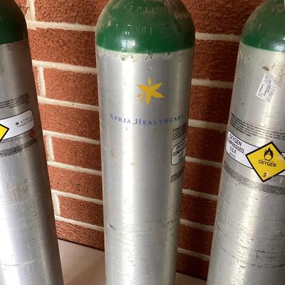 Sale Photo Thumbnail #370: A set of three aluminum compressed oxygen tanks labeled for medical/U.S.P. use, featuring CGA 870 post valves. Includes markings from Apria Healthcare and Sherwood valves. Shows typical surface scuffs, wear, and sticker residue from prior use and transpor