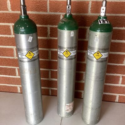 Sale Photo Thumbnail #368: A set of three aluminum compressed oxygen tanks labeled for medical/U.S.P. use, featuring CGA 870 post valves. Includes markings from Apria Healthcare and Sherwood valves. Shows typical surface scuffs, wear, and sticker residue from prior use and transpor