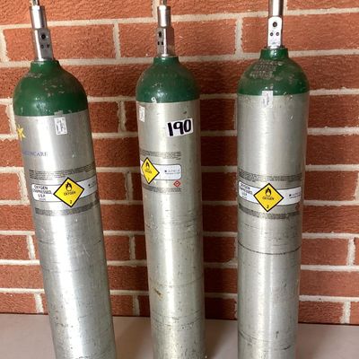Sale Photo Thumbnail #372: Set of three medical compressed oxygen cylinders with Sherwood valves and Apria Healthcare labels. Aluminum bodies with green tops. Used condition with visible surface scratches, scuffs, and sticker residue. Hydrotest dates and specifications stamped on c