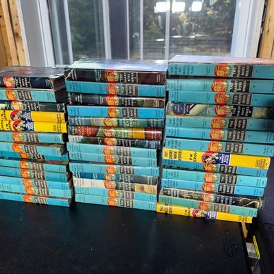 Sale Photo Thumbnail #132: Collection of approximately 46 Hardy Boys mystery books by Franklin W. Dixon, Grosset & Dunlap. Mostly blue-spine picture-cover editions, plus yellow-spine "The Hardy Boys Stories" editions and several with dust jackets. Volumes range from #1 The Tower Tr
