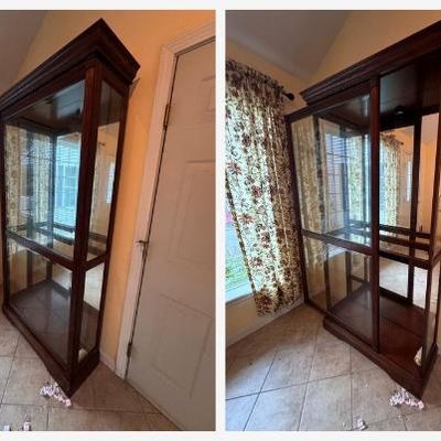 Sale Photo Thumbnail #147: Two matching large solid oak curio display cabinets in a rich cherry-tone finish. Each features:
• Sliding front glass door with lock
• Glass side panels and mirrored back
• Built-in top lighting (two puck lights) with plug-in cord
• Crown molding
