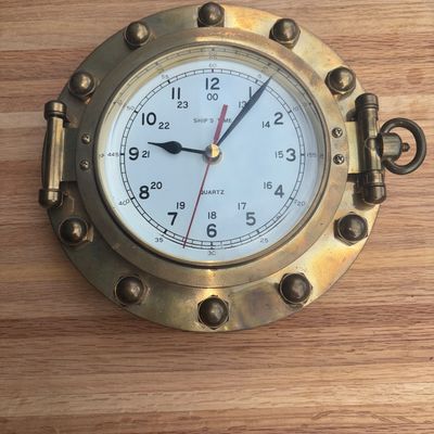 Sale Photo Thumbnail #39: Nautical style brass wall clock designed like a ship's porthole with decorative bolt accents and a top hanging loop. Features a white face marked 'SHIP'S TIME' and 'QUARTZ' with 12-hour and 24-hour military time markings. Shows natural age patina and tarn