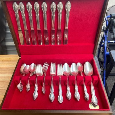 Sale Photo Thumbnail #40: Vintage silver-plated flatware set featuring a floral relief pattern on the handles. Includes dinner knives, forks, salad forks, soup spoons, and teaspoons. Housed in a wooden McGraw tarnish-proof silverware chest lined with red felt. Flatware shows light