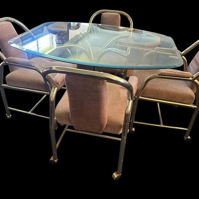 Sale Photo Thumbnail #670: 48"L × 42"W × 28.5"T. Set of 4 chairs. Vintage 5-piece casual dining/game set featuring a rounded glass top table on tubular brass legs  paired with 4 matching brass frame armchairs with mauve/taupe fabric upholstery on rolling caster wheels. 48"L × 42