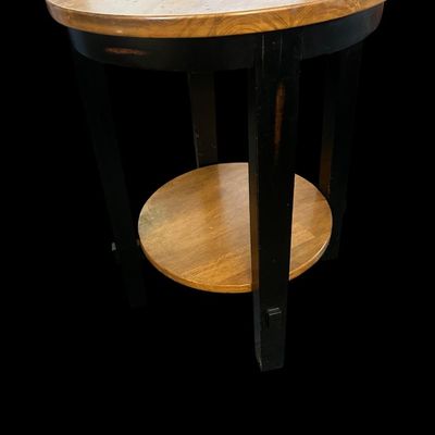 Sale Photo Thumbnail #740: 26.00 Tall 19.50 Round Round wood end table with a warm natural wood grain top and lower shelf paired with distressed black square legs. 26.00 Tall 19.50 Round  