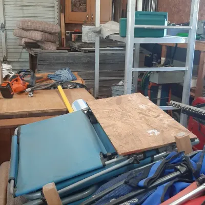 Assorted workshop items and outdoor gear, including folding camp chairs, a blue lawn chair, a small power tool, and metal shelving units.