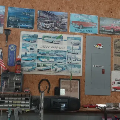 Garage wall display featuring vintage Chevrolet-themed art, signs, posters, along with tools, a portable boombox, and small storage...