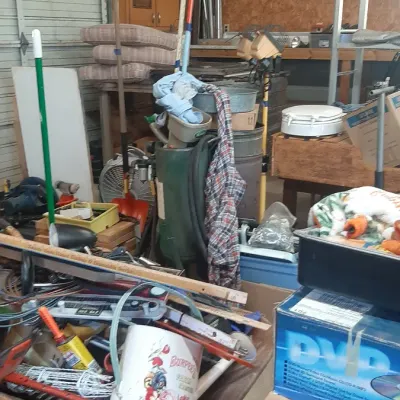 Assorted workshop items, lawn tools, a wheelbarrow filled with supplies, and stacked storage boxes inside a garage.