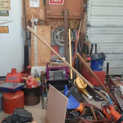 Assorted workshop tools, lawn equipment, gas cans, and garage signs in a home garage space.