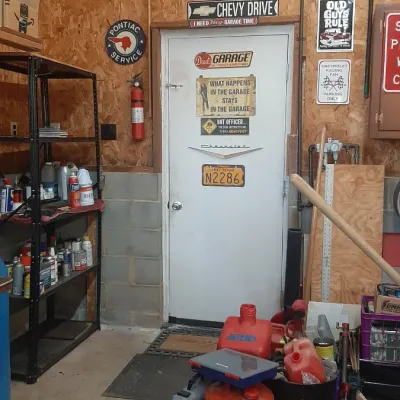 Workshop garage interior filled with automotive signs, tools, gas cans, and shelving units.