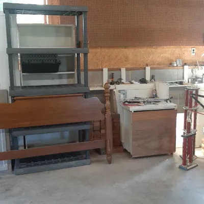 Workshop storage items including a black plastic shelving unit, a wooden headboard, a cabinet base, and a large multi-tiered trophy.
