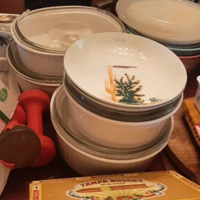 Collection of household goods including CorningWare casseroles, a Tampa Nugget cigar box, cookware, and hand weights.