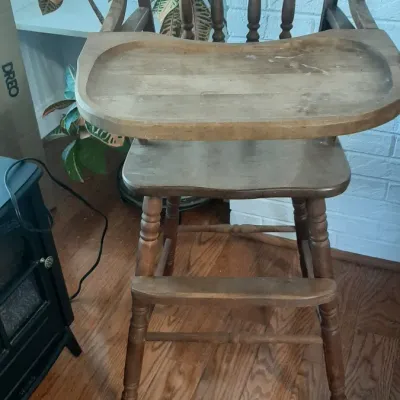 Vintage wooden high chair with a spindle back and flip-over tray, showing light surface wear.