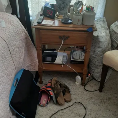 Traditional wooden nightstand with a single drawer, housing a ceramic table lamp, digital alarm clock, and various bedside accessories.