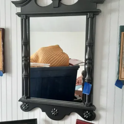 Black painted vintage wall mirror with a broken pediment top, center finial, turned side columns, and floral motifs at the base.