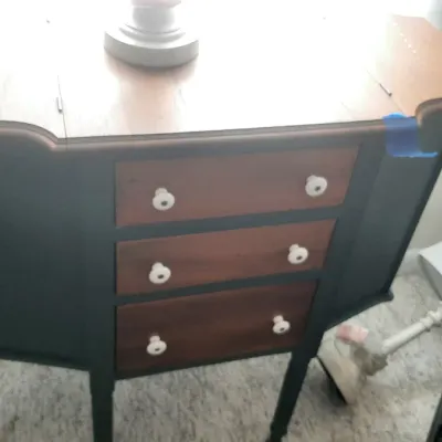 Vintage drop-leaf sewing cabinet painted dark blue with natural wood drawer fronts and white ceramic knobs.