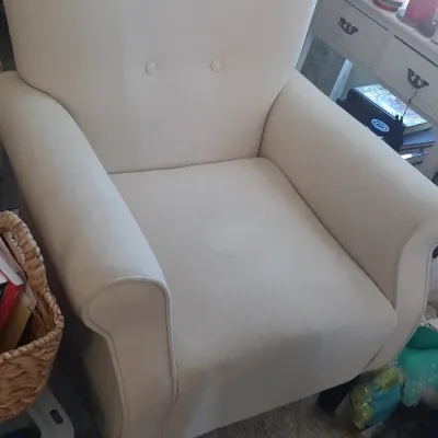 Contemporary cream-colored upholstered armchair featuring a button-tufted backrest and dark wooden legs.
