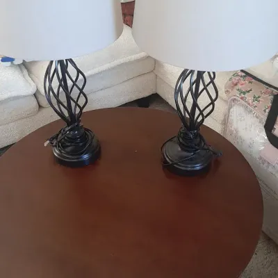 Pair of contemporary table lamps featuring twisted black wrought iron openwork bases and white drum shades, displayed on a round wooden...