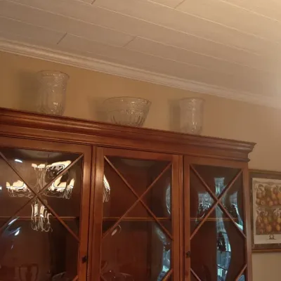 Large wooden display hutch with glass doors featuring diagonal mullions, topped with crystal vases and a bowl.