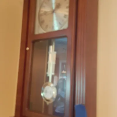 Traditional wooden regulator wall clock featuring a brass pendulum and Roman numeral dial behind glass.
